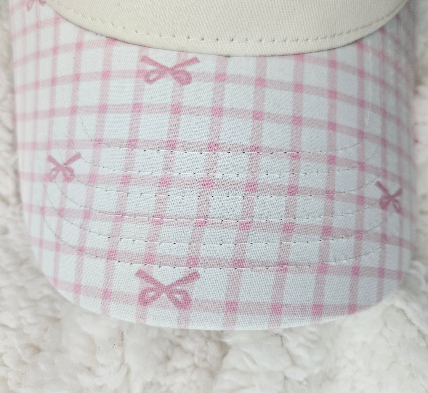 Close-up of a pink and white checkered bill of hat with bows on a textured surface