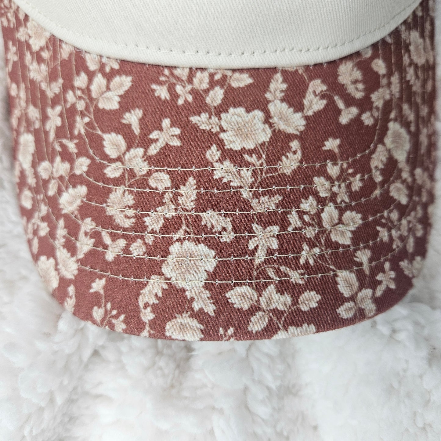 Close-up of a bill of hat with white flowers on a brown background.
