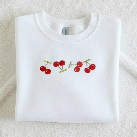 White sweatshirt with red cherry design on a textured surface