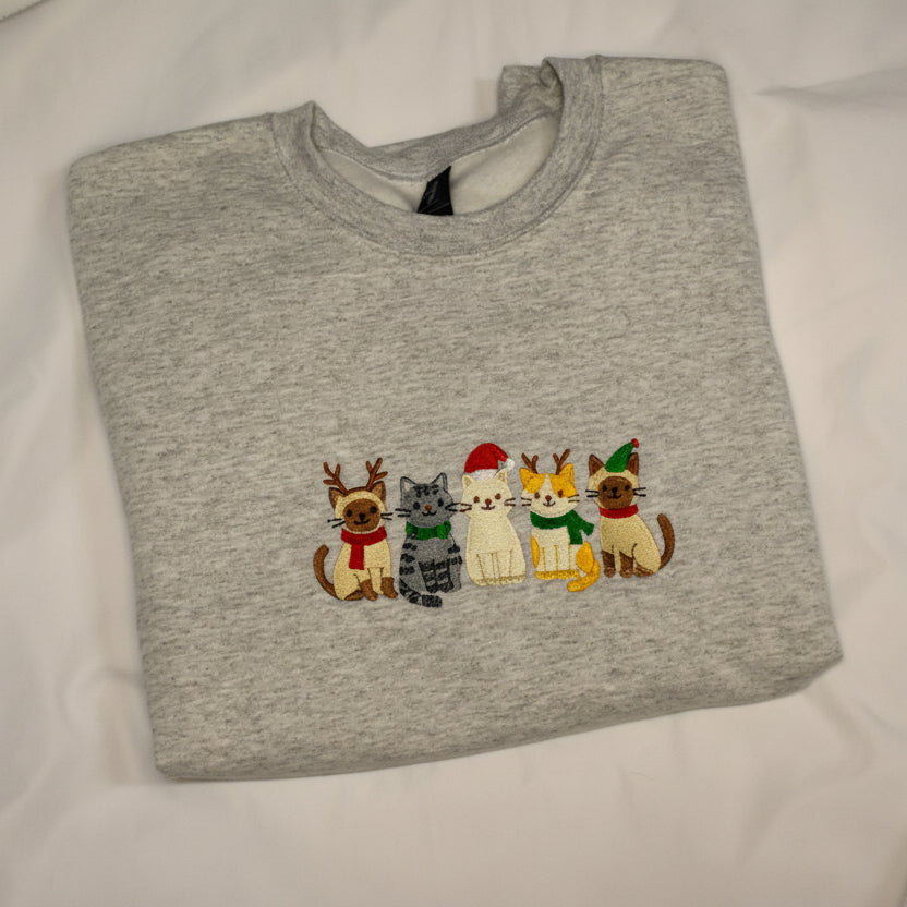Folded ash gray sweatshirt with embroidered cats design on a white background