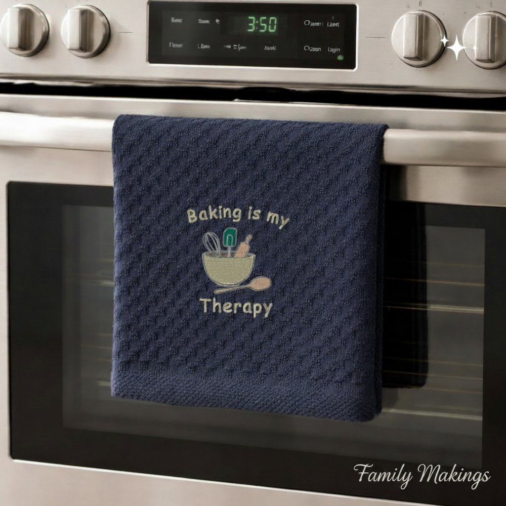 Black towel with 'Baking is my Therapy' text hanging on a silver oven.