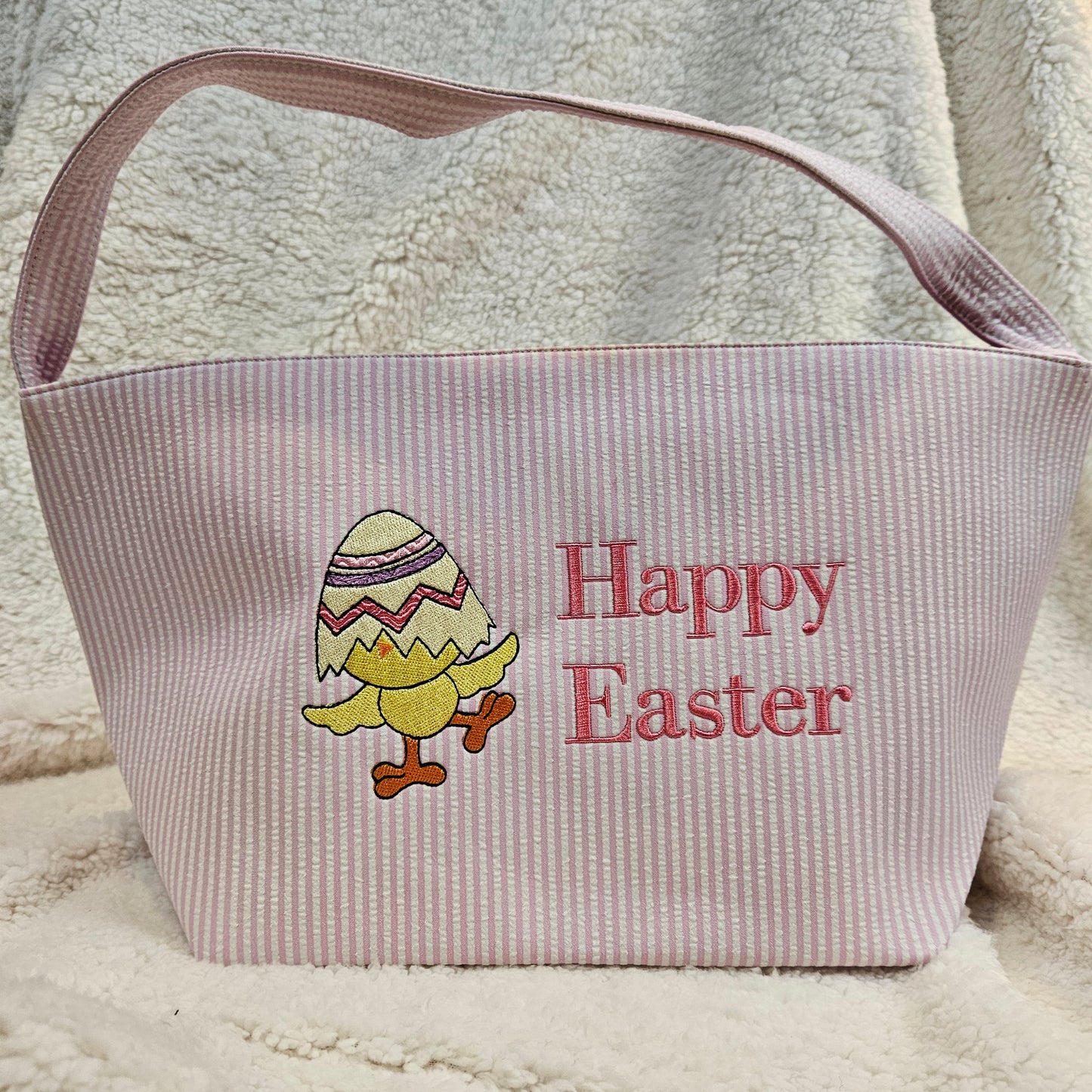 Pink stripped basket with embroidered Easter design and text on a textured surface