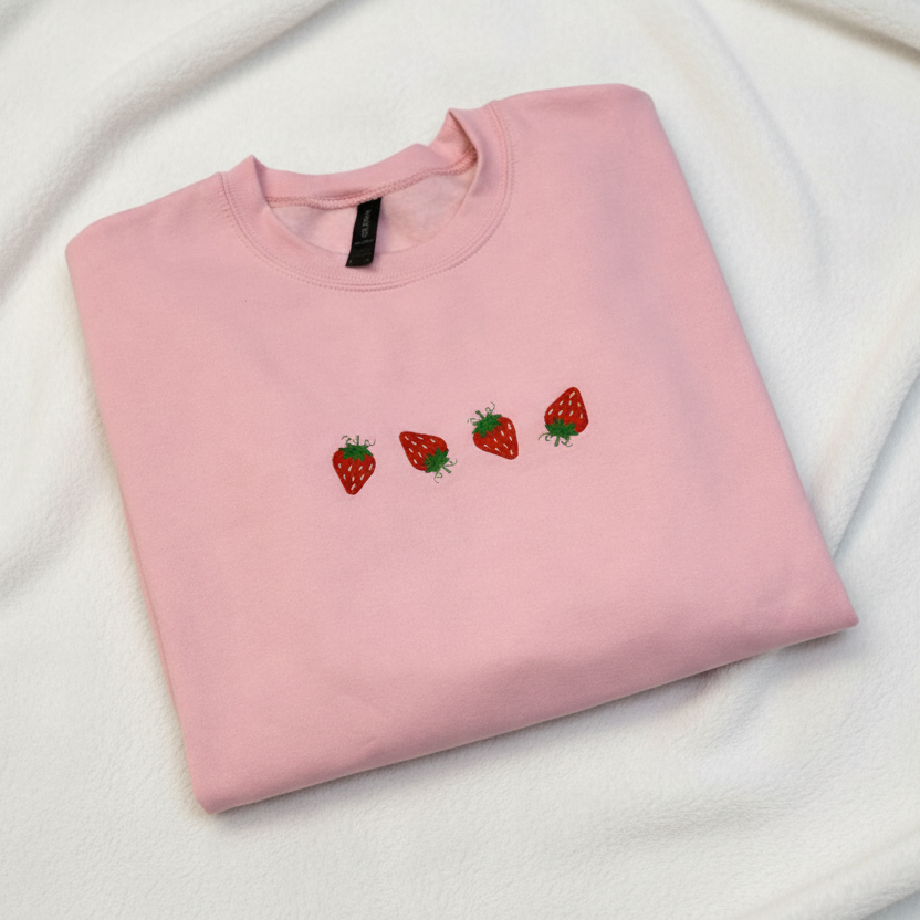 Folded Light pink sweatshirt with embroidered strawberries on a white background