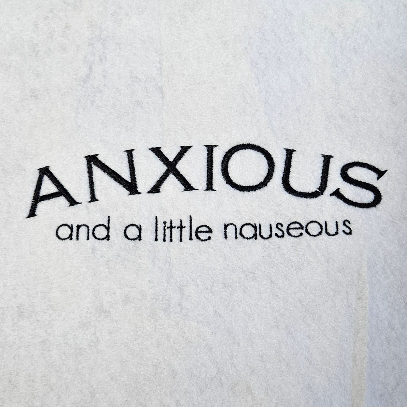 Embroidered text 'ANXIOUS and a little nauseous' on a white background