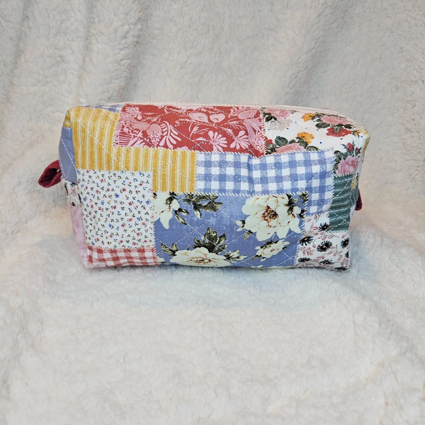 Folded patchwork pouch with floral and plaid patterns on a light gray background