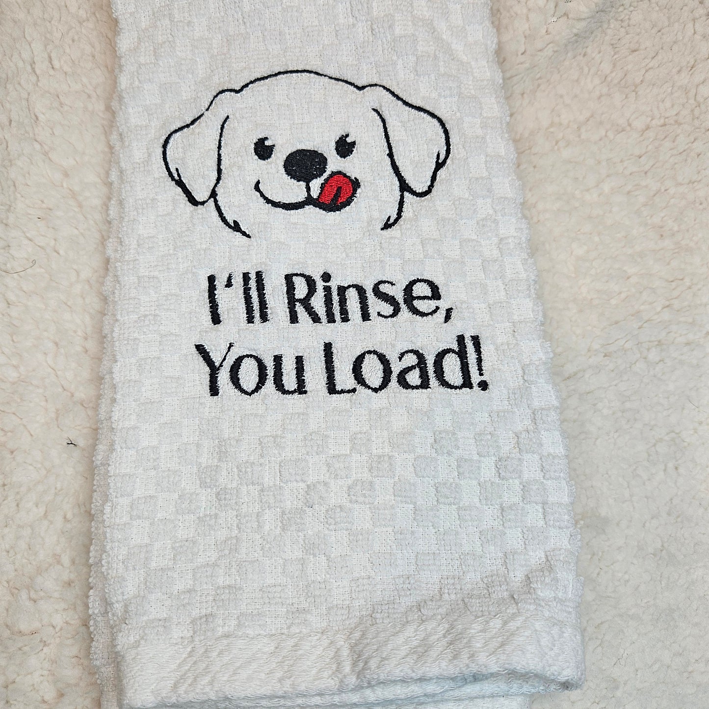 White towel with a dog illustration and text 'I'll Rinse, You Load!' on a textured surface.