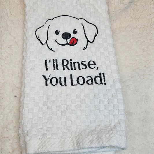 White towel with a dog illustration and text 'I'll Rinse, You Load!' on a textured surface.