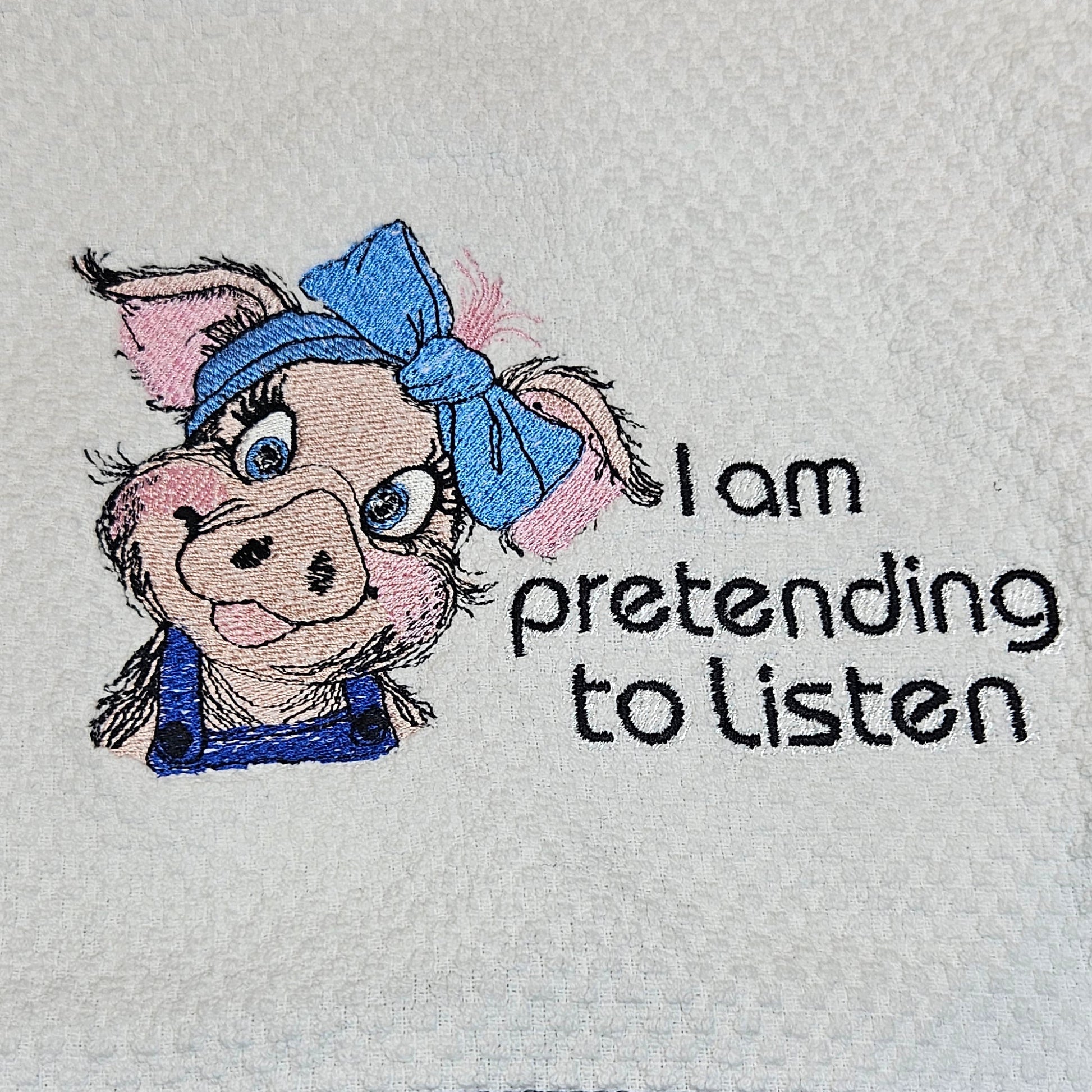 Towel with embroidered character and text 'I am pretending to listen' on a textured surface.
