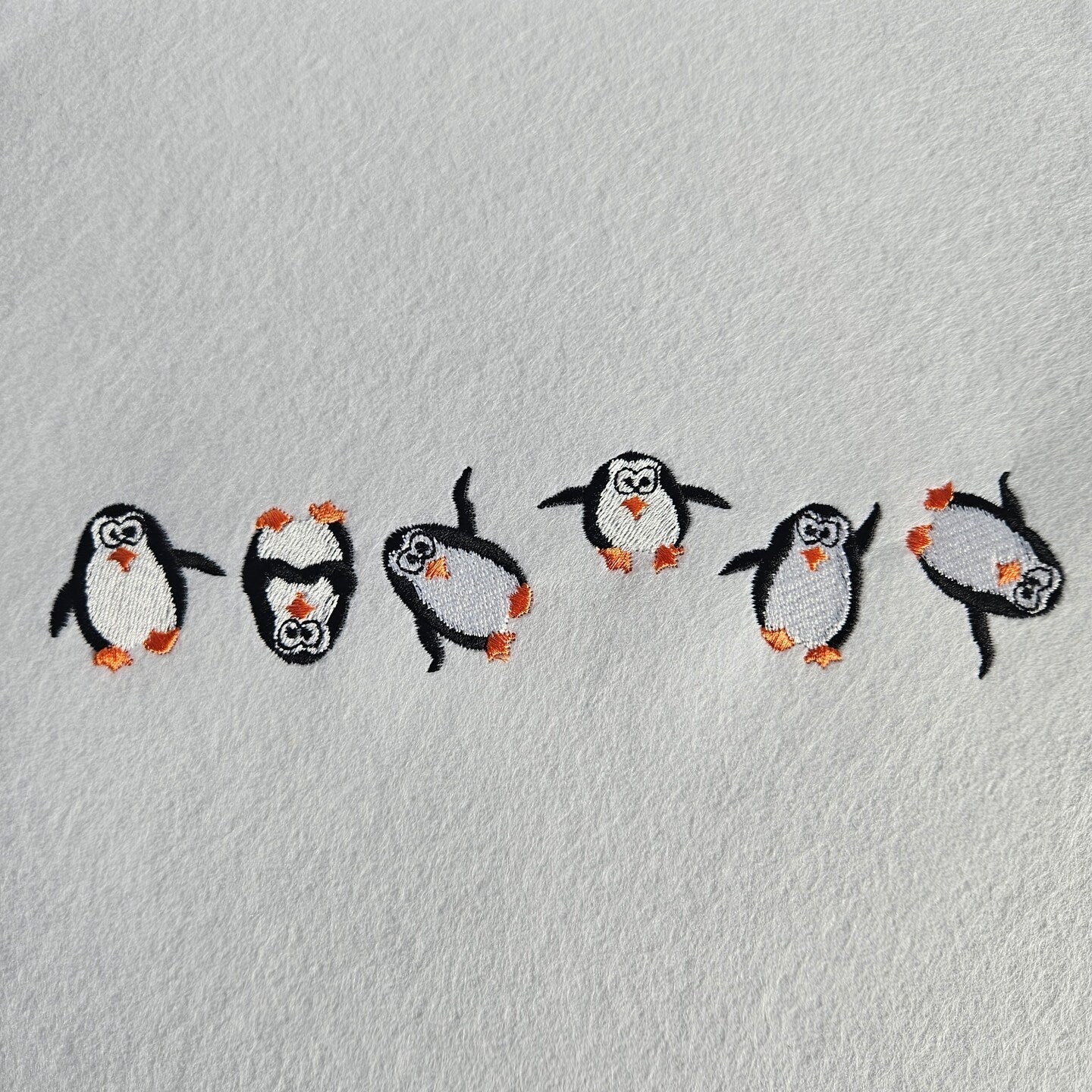 Embroidered penguin designs on a textured gray background