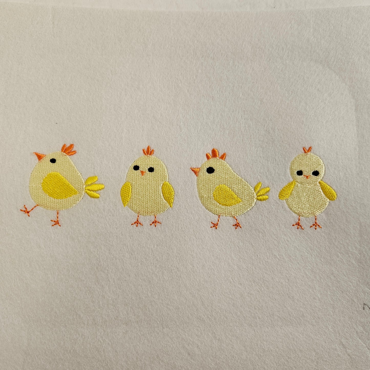 Four embroidered chicks on a textured beige fabric background
