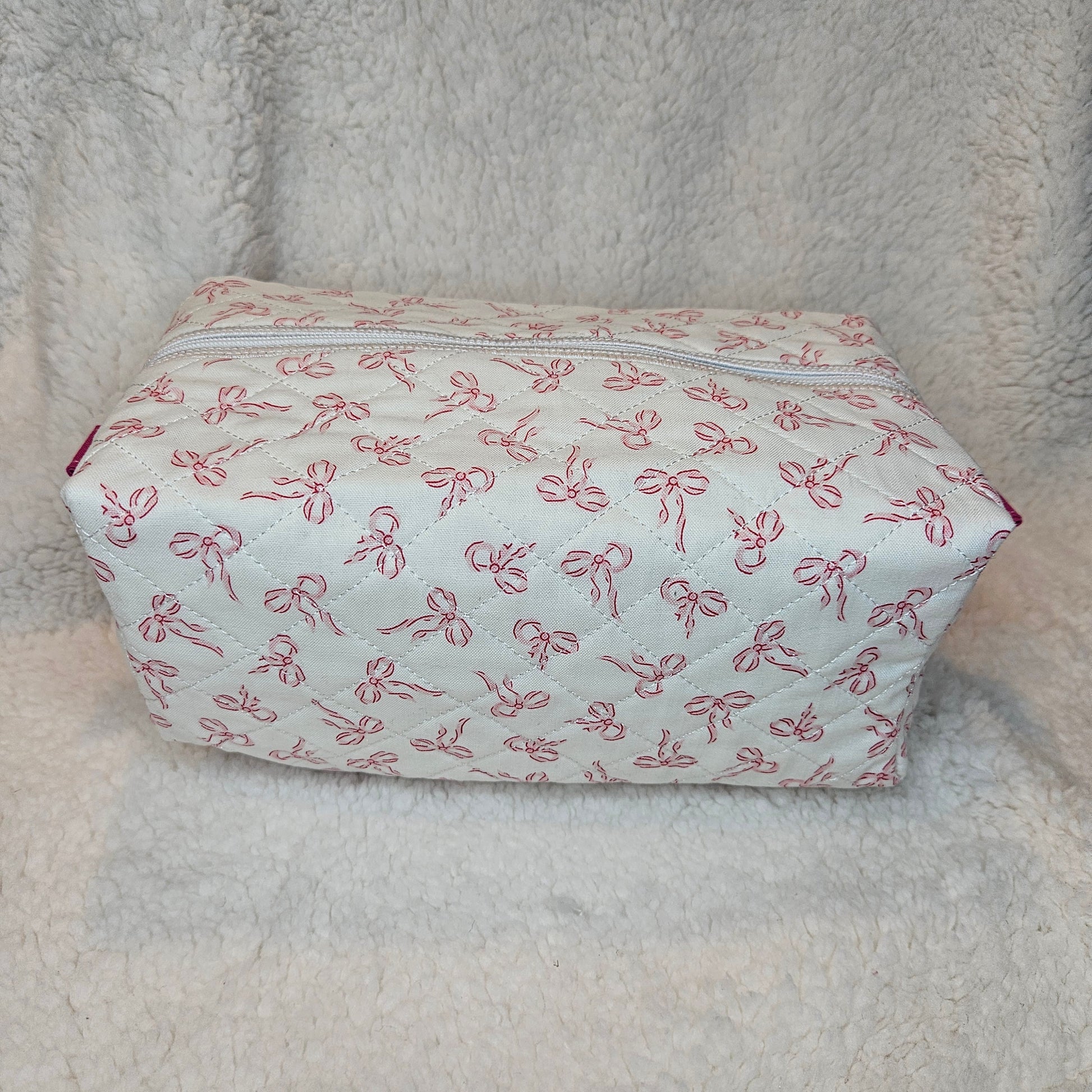 Small rectangular pouch with pink bow pattern on a textured beige surface