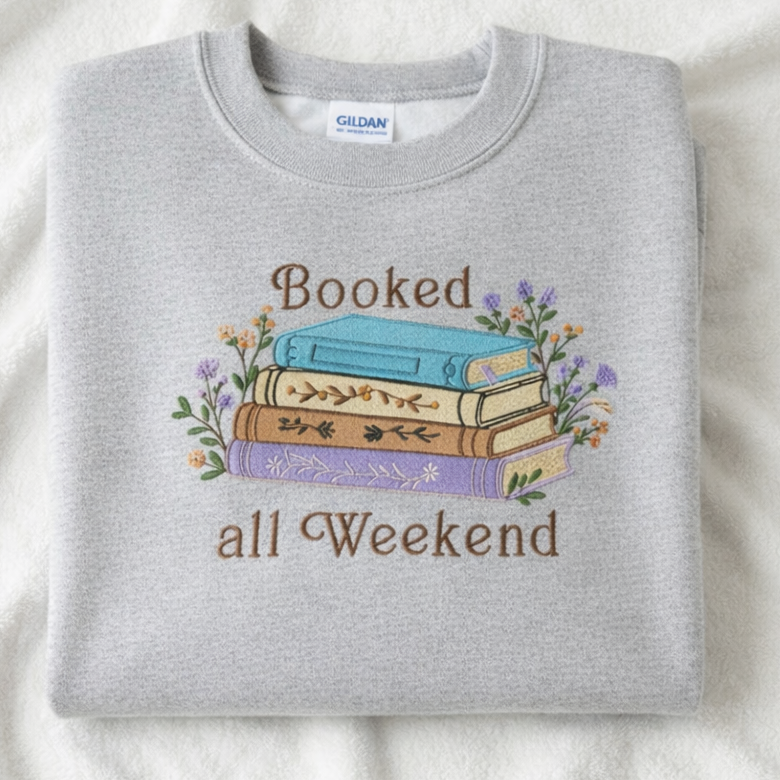 Folded ash gray sweatshirt with 'Booked all Weekend' text and book design on a white background