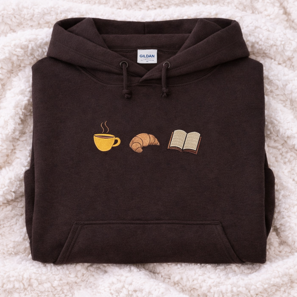 Folded dark chocolate hoodie with coffee cup, croissant, and book design on a textured surface