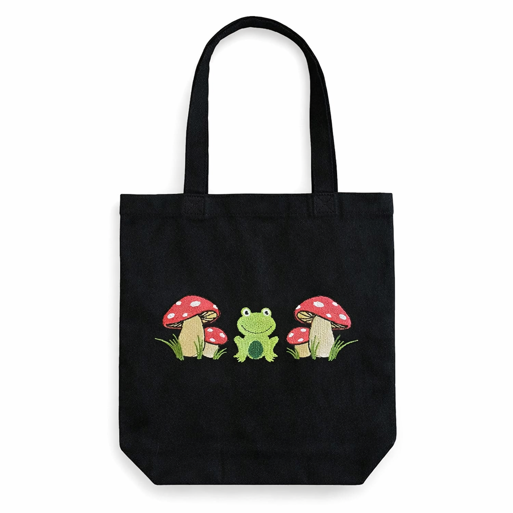 Black tote bag with a frog and mushroom design on a white background
