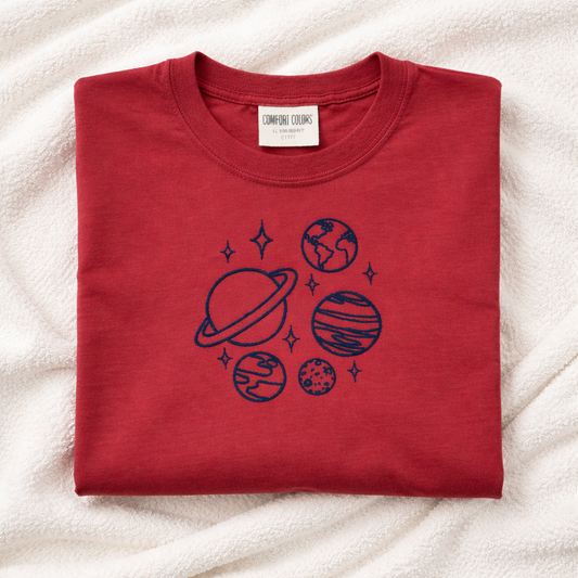 Folded crimson t-shirt with space-themed design on a light background