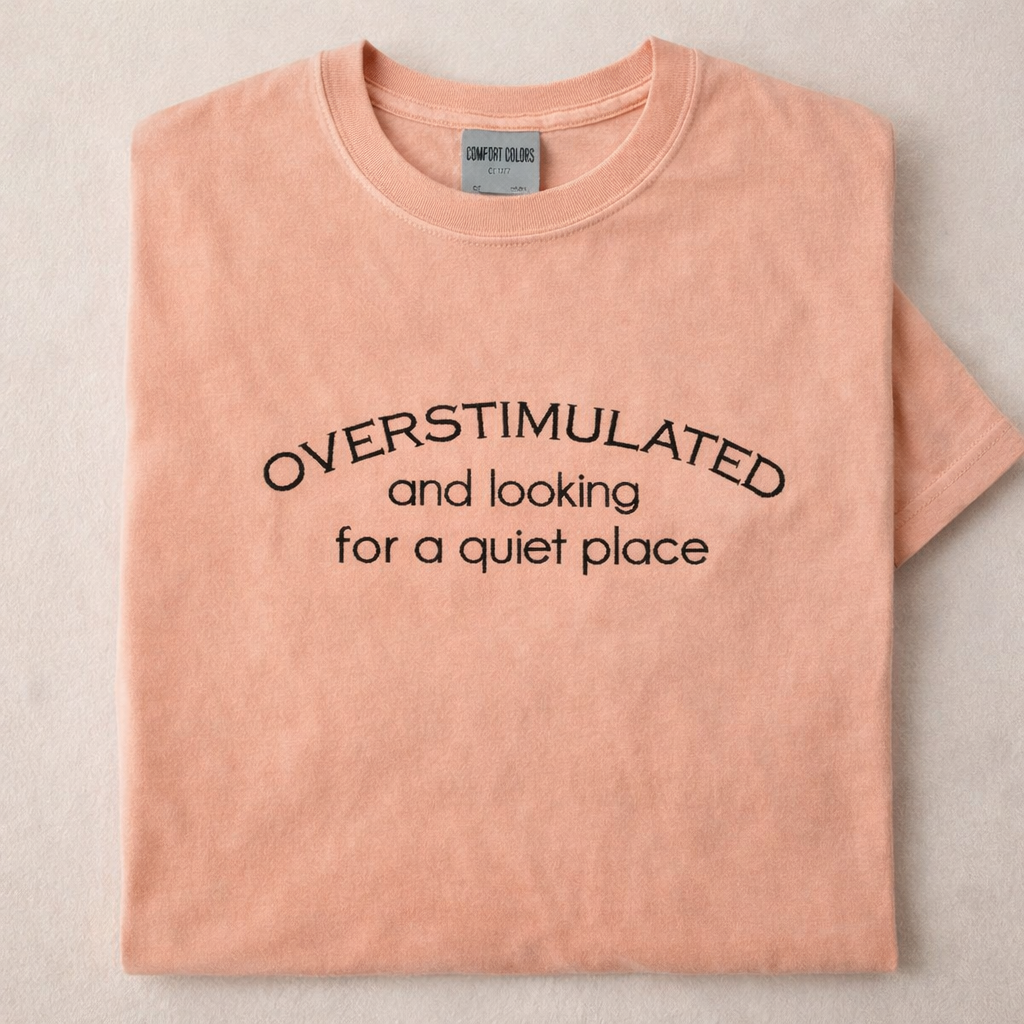 Peachy t-shirt with embroidered text 'Overstimulated and looking for a quiet place' on a beige background