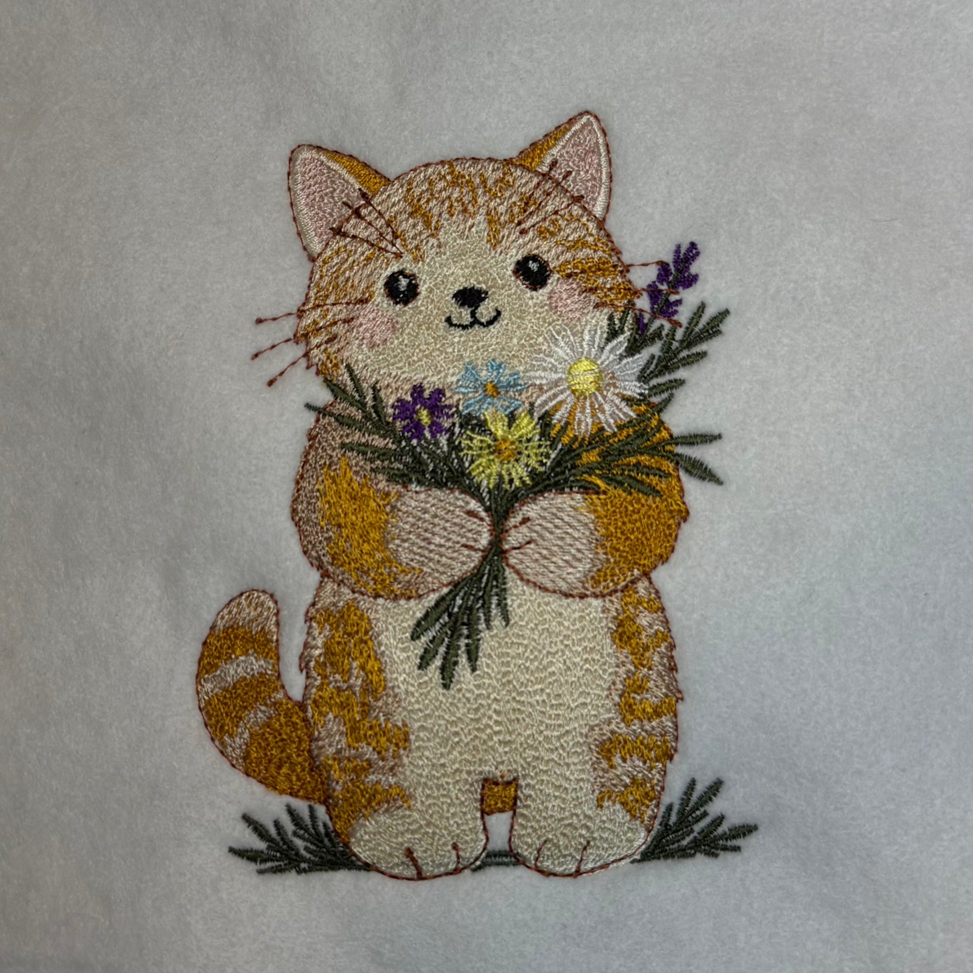Embroidered design of a cat holding flowers on a white background