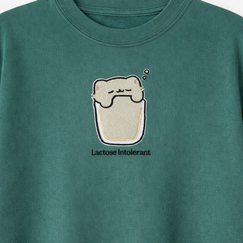 Emerald t-shirt with an embroidered cartoon cat in a glass of milk and 'Lactose Intolerant' text