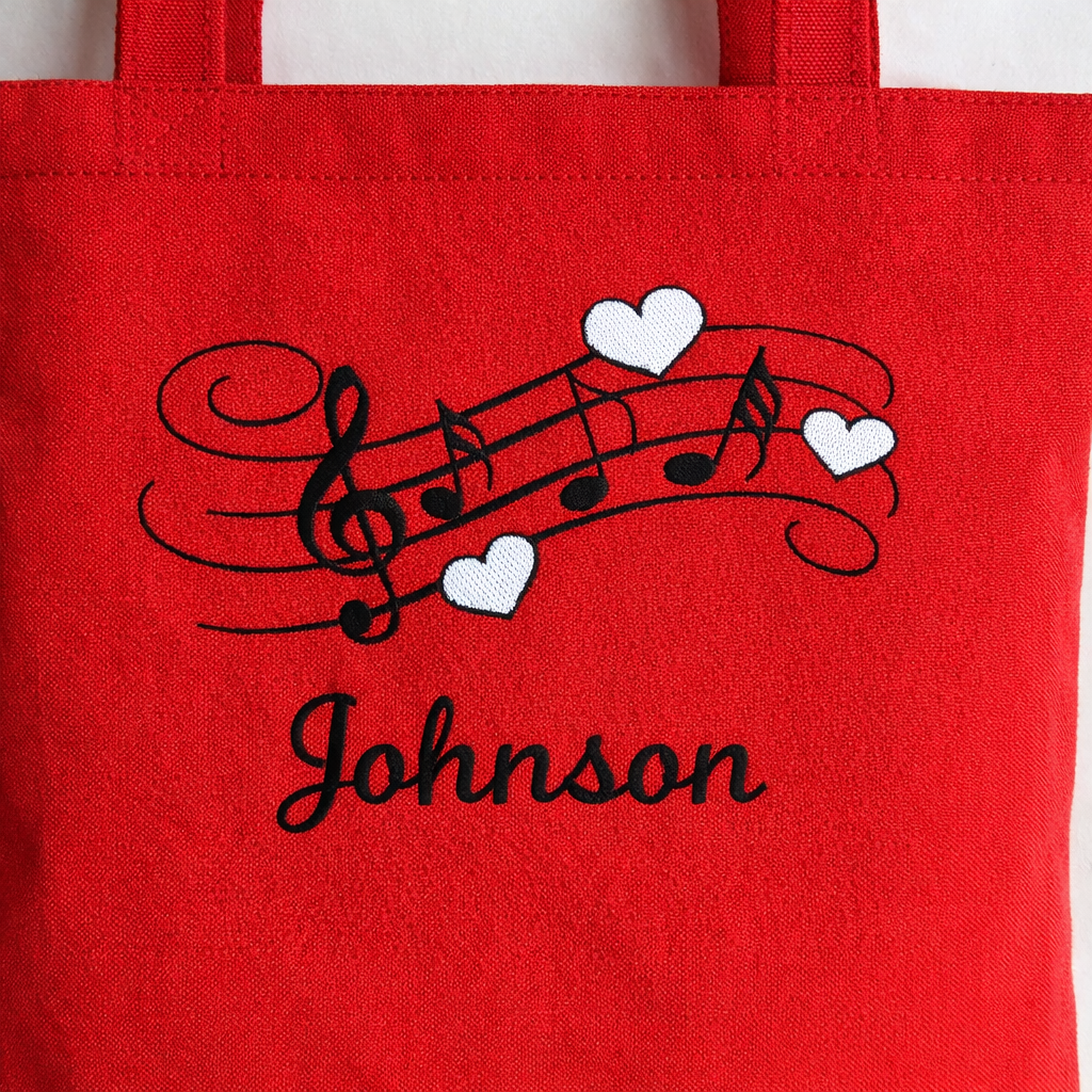Red tote bag with musical notes and hearts design and 'Johnson' text.