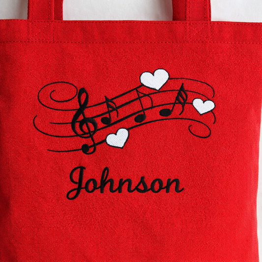 Red tote bag with musical notes and hearts design and 'Johnson' text.