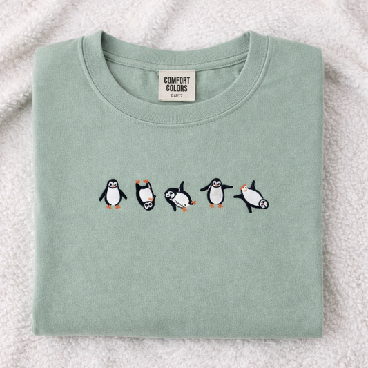 Folded sage t-shirt with penguin design on a textured surface