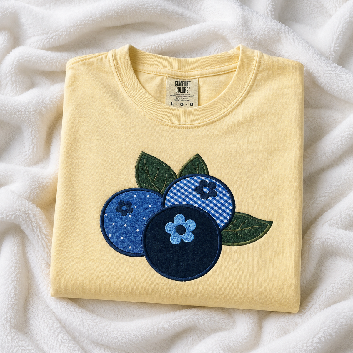 Folded butter t-shirt with blue and green appliqué design on a white fabric background