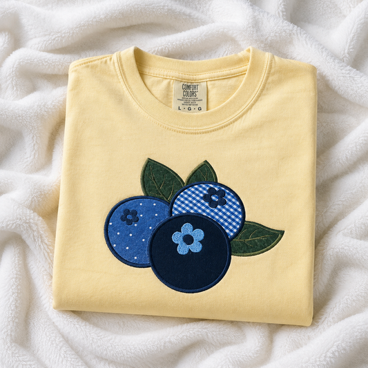 Folded butter t-shirt with blue and green appliqué design on a white fabric background