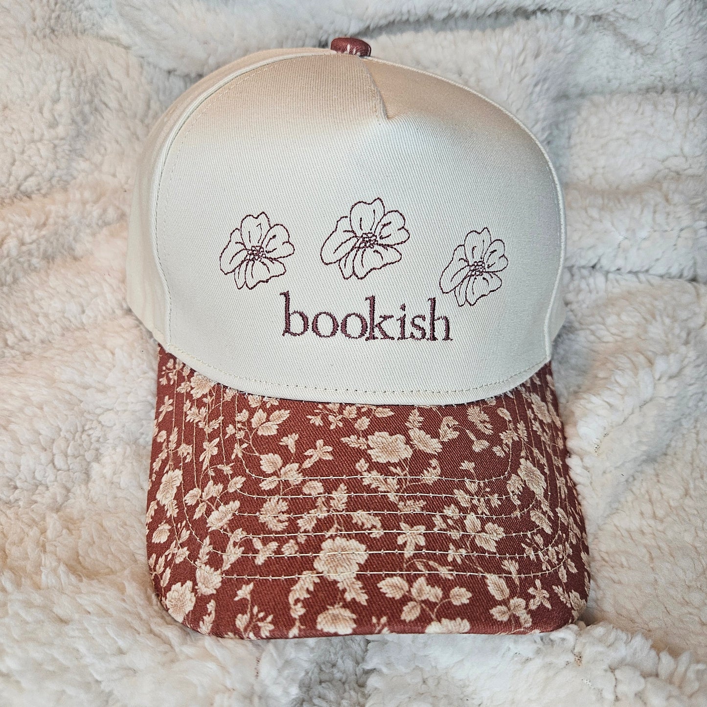Floral-patterned cap with 'bookish' text on a textured surface