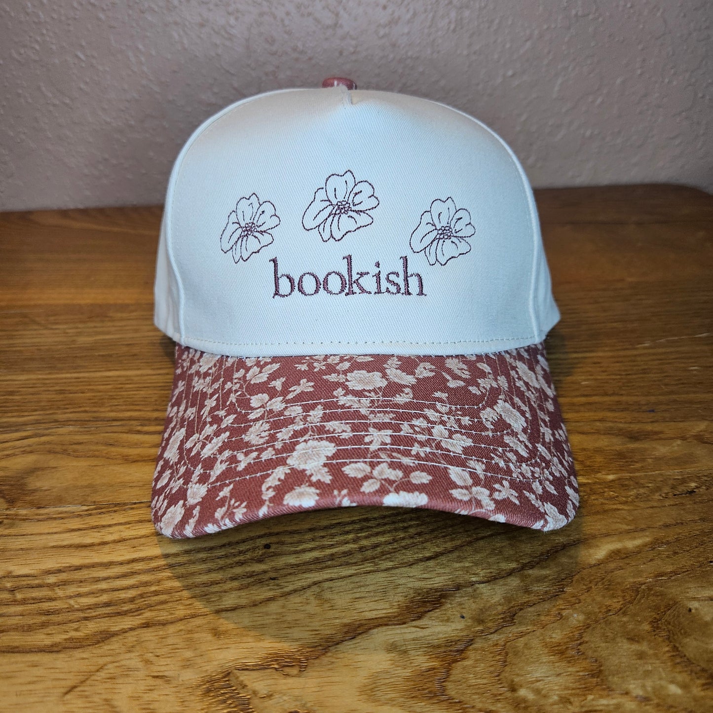 Trucker hat with 'bookish' text and floral design on a wooden surface