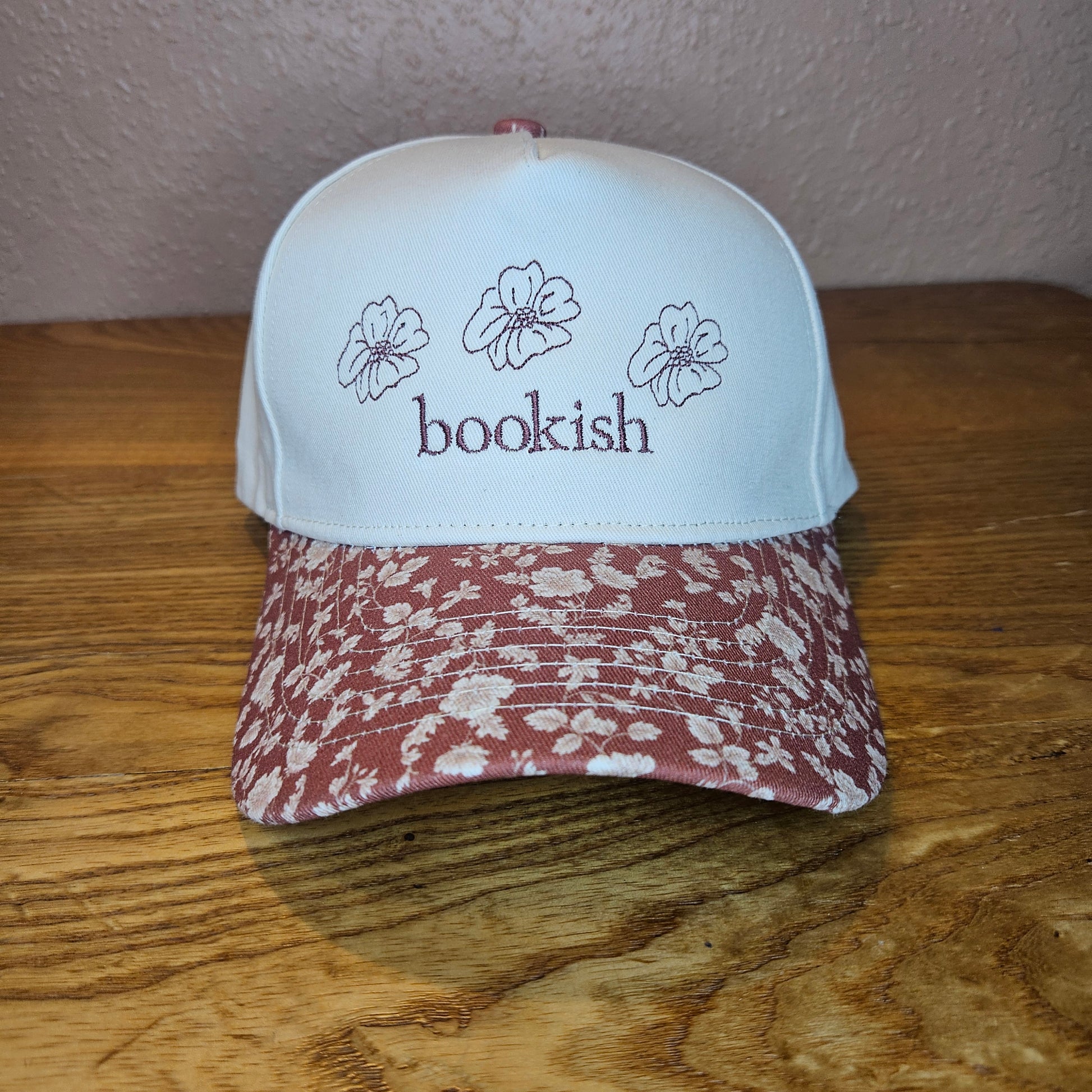 Trucker hat with 'bookish' text and floral design on a wooden surface