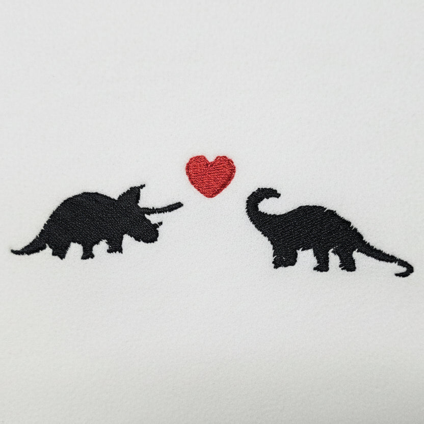 Embroidered design of two dinosaurs with a red heart on a light gray fabric.