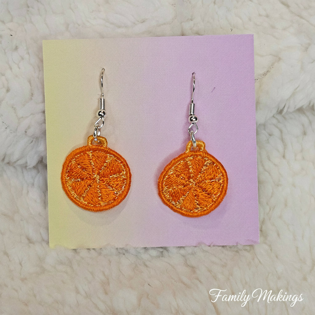 Embroidered orange slice earrings with silver posts on a card 
