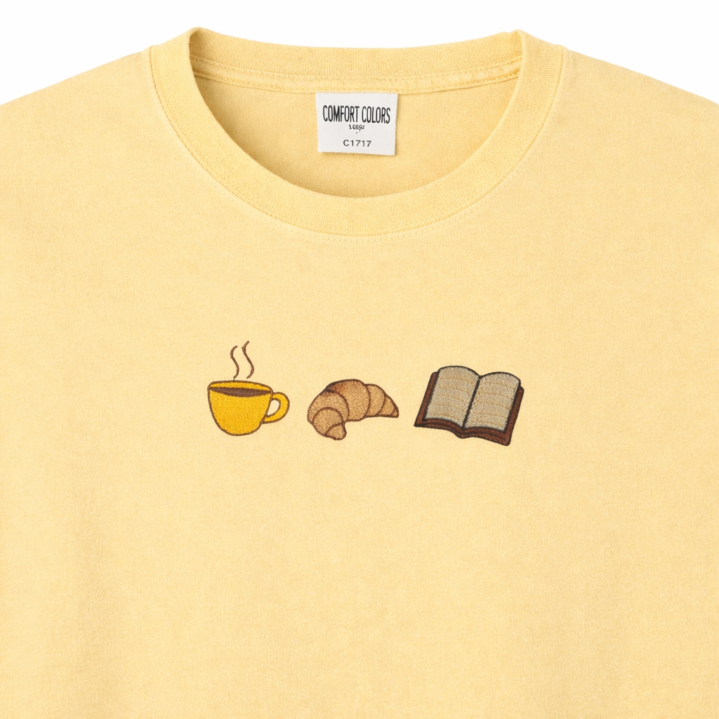 Butter t-shirt with coffee cup, croissant, and book embroidery design on a white background.