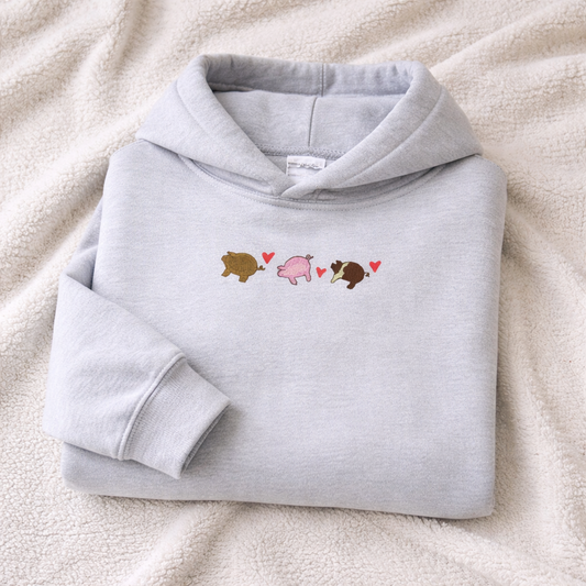 Folded ash gray hoodie with pigs and hearts design on a white blanket