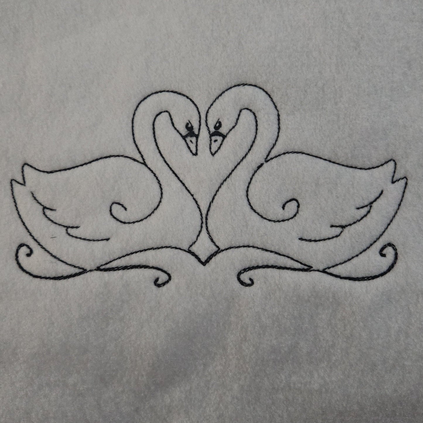 Embroidered design of two swans forming a heart shape on a white background
