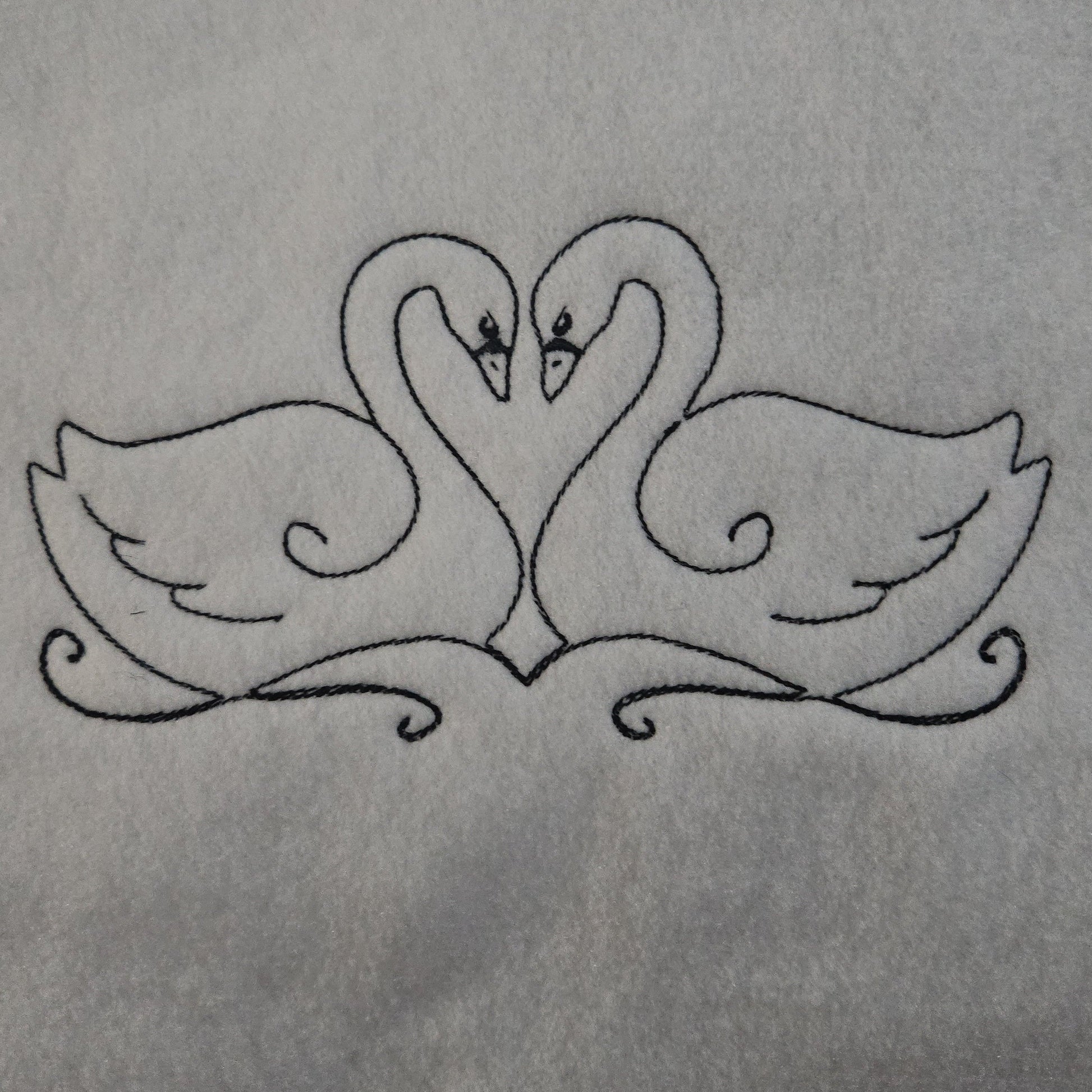 Embroidered design of two swans forming a heart shape on a white background