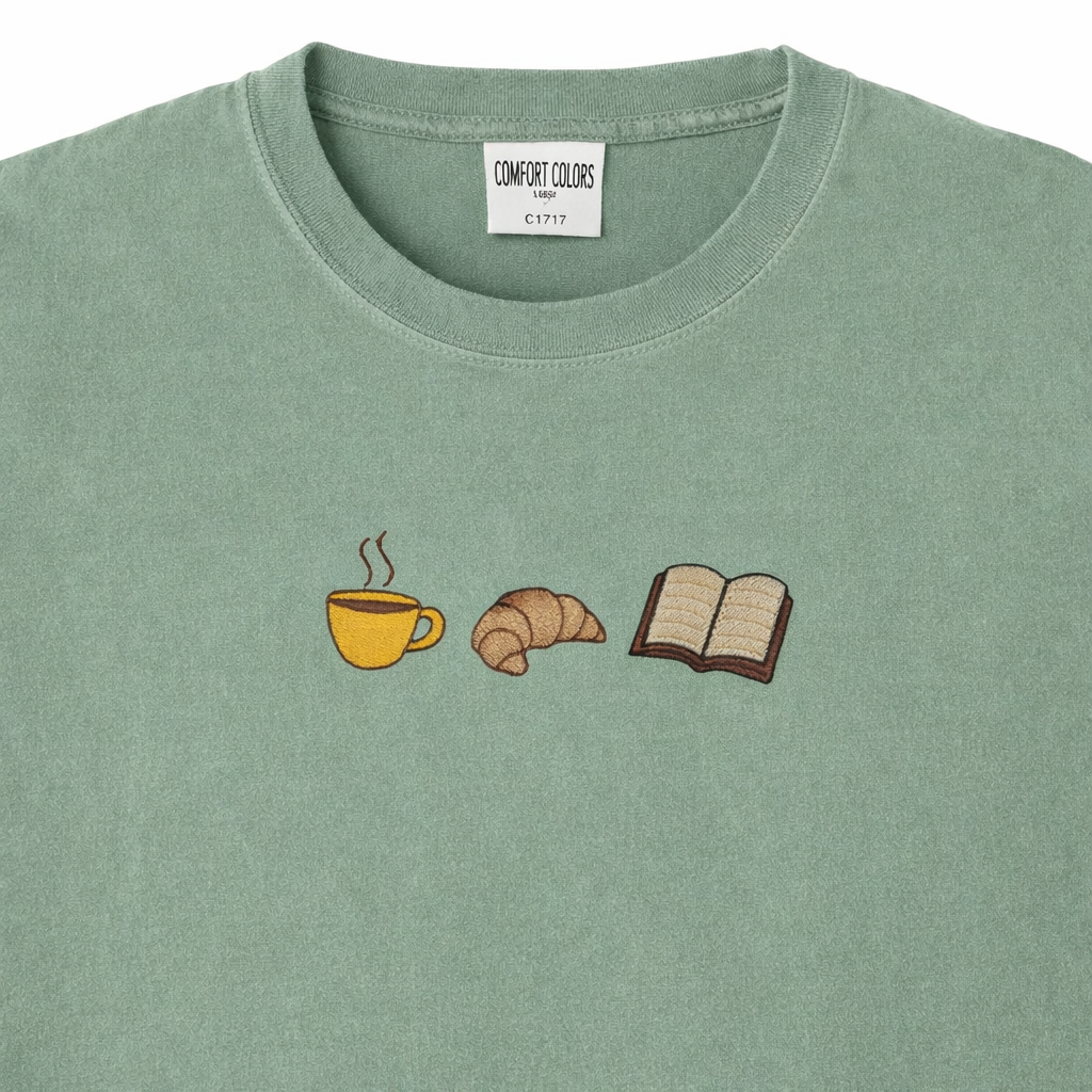 Sage t-shirt with embroidered coffee cup, croissant, and book design.