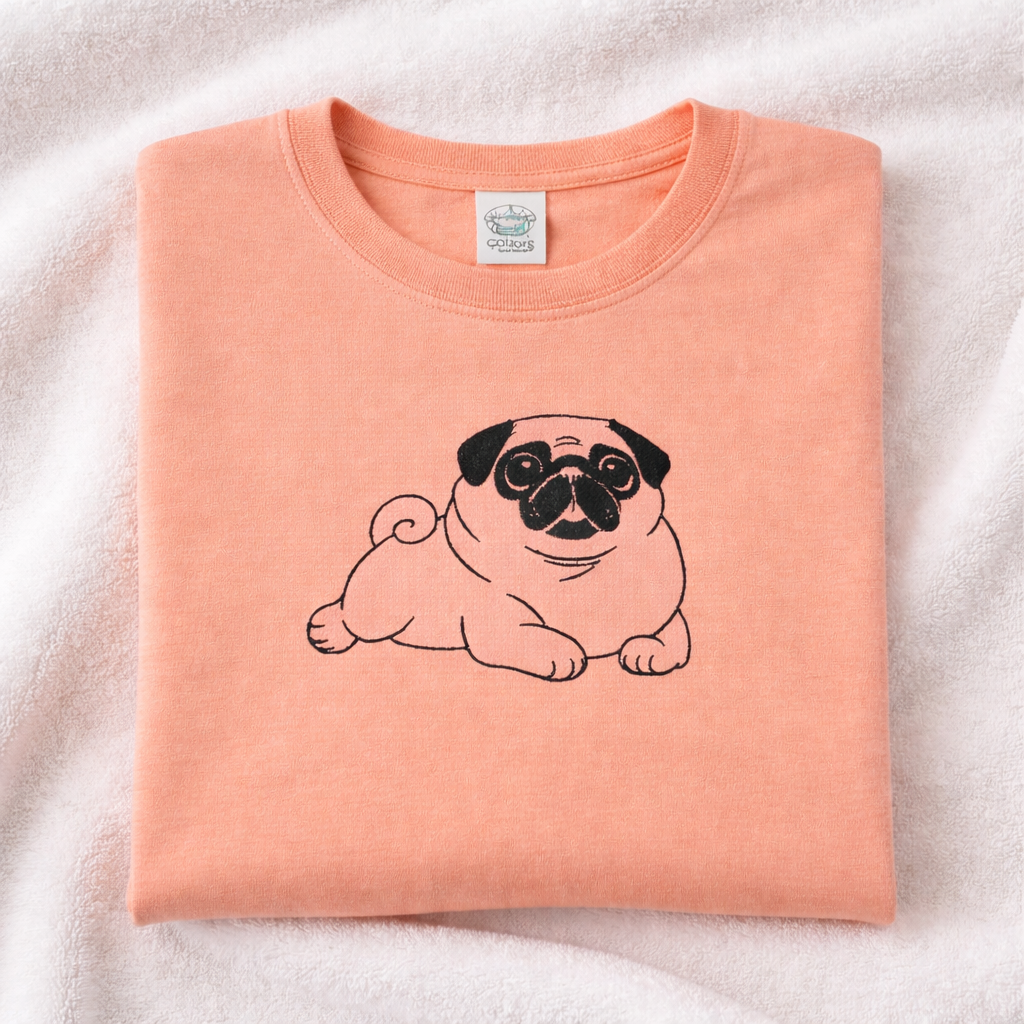 Folded peachy t-shirt with a black pug design on a light pink background
