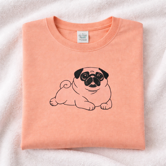 Folded peachy t-shirt with a black pug design on a light pink background