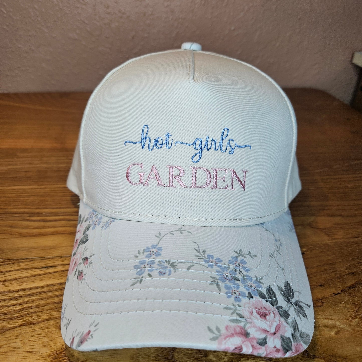 Floral-patterned cap with embroidered text on a wooden surface