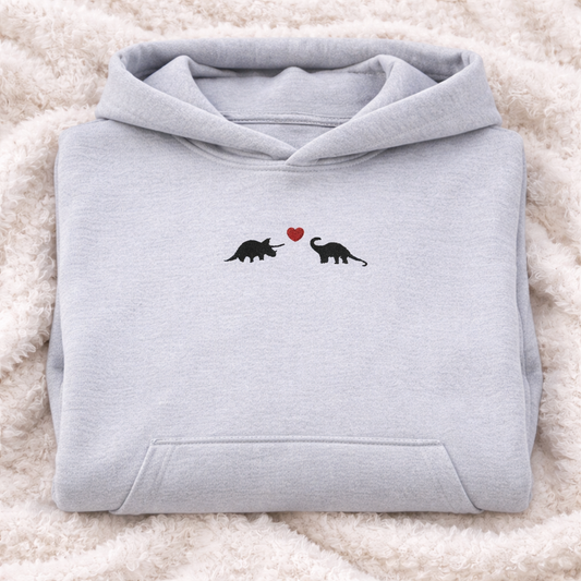 Folded Ash gray hoodie with a heart and dinosaur design on a fluffy white surface