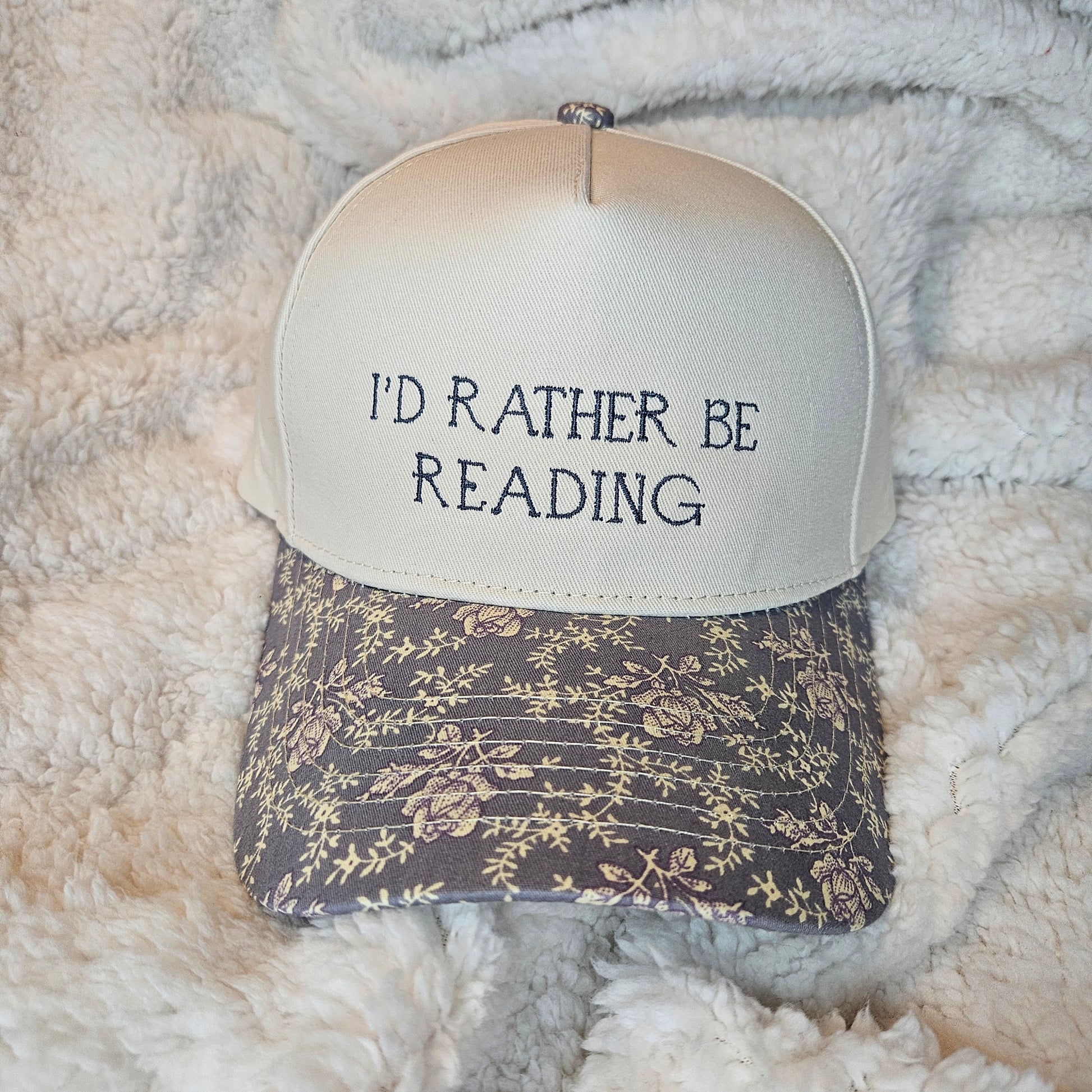Trucker hat with 'I'd Rather Be Reading' text on a textured surface