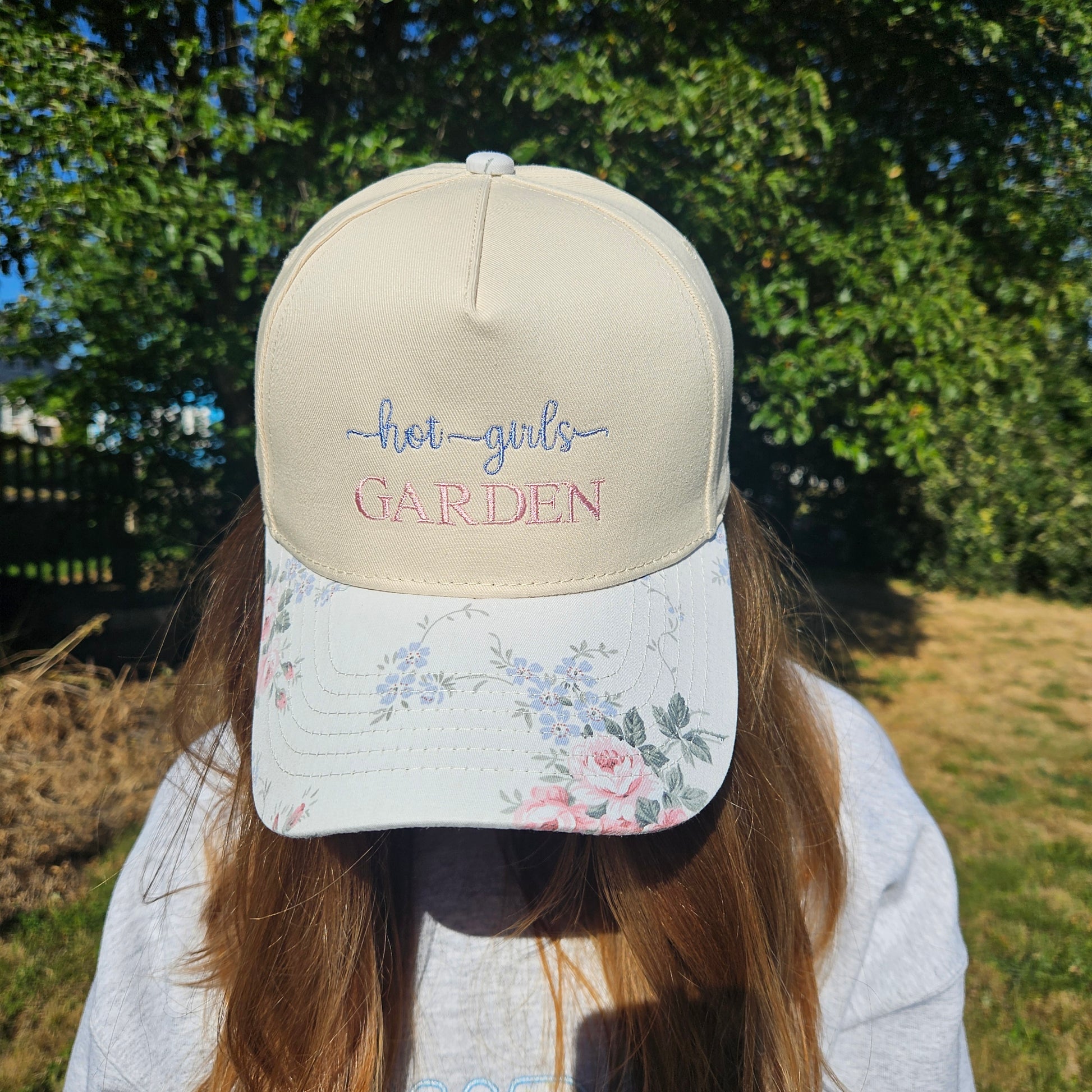 Person wearing a cap with floral design and text, standing outdoors with trees in the background
