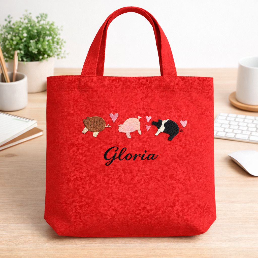 Red tote bag with embroidered designs and 'Gloria' text on a desk.
