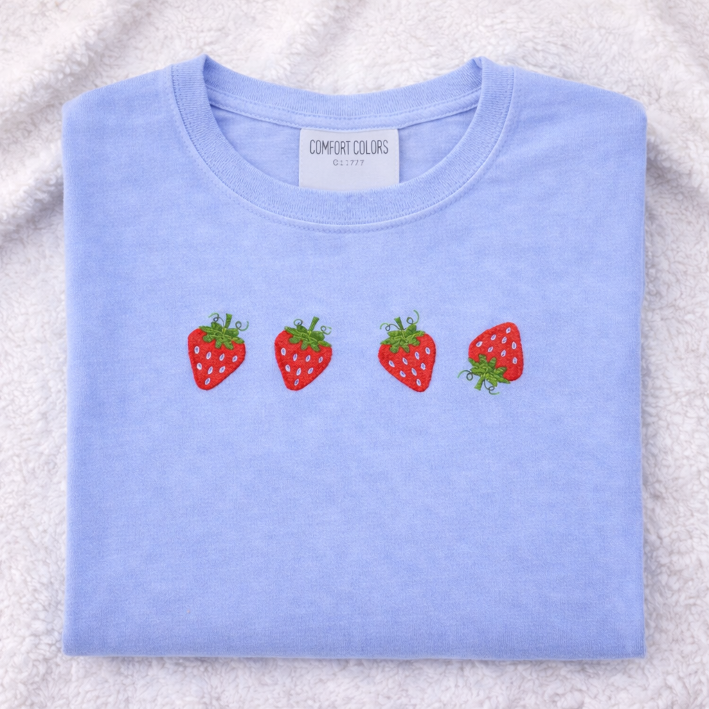 Folded Hydrangea colored t-shirt with strawberry designs on a textured surface