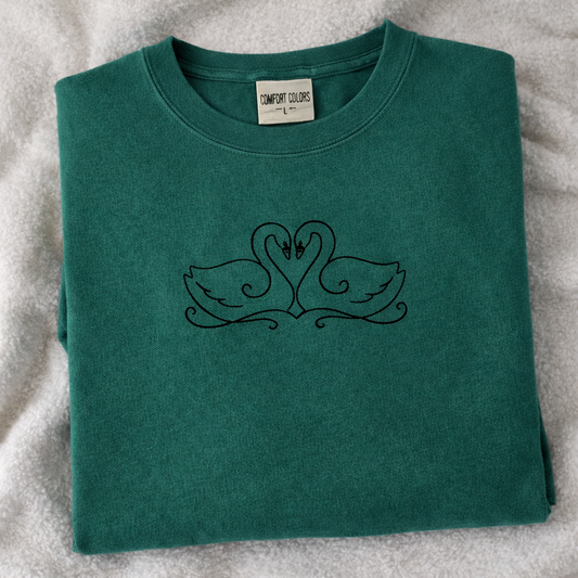 Folded emerald t-shirt with black Swan design on a white fabric background