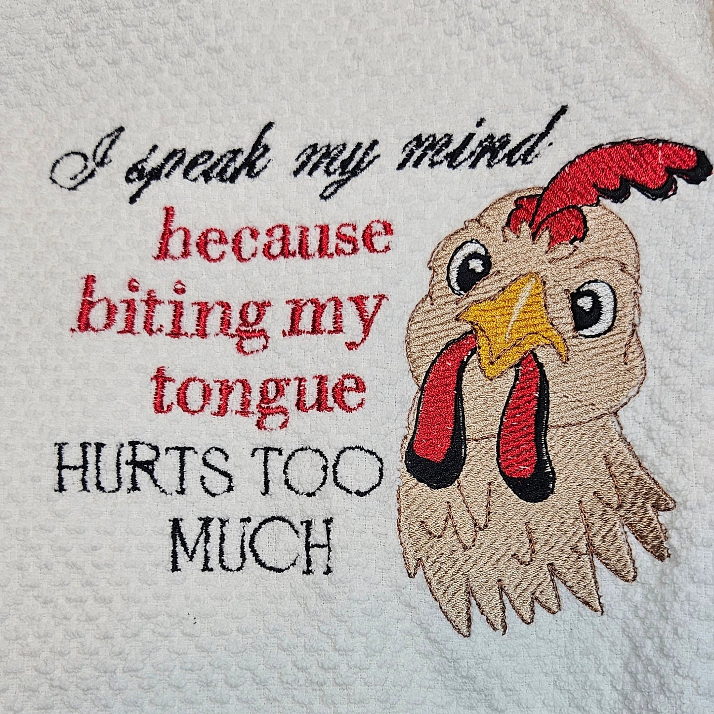 Embroidered towel with rooster design and humorous text on a textured surface