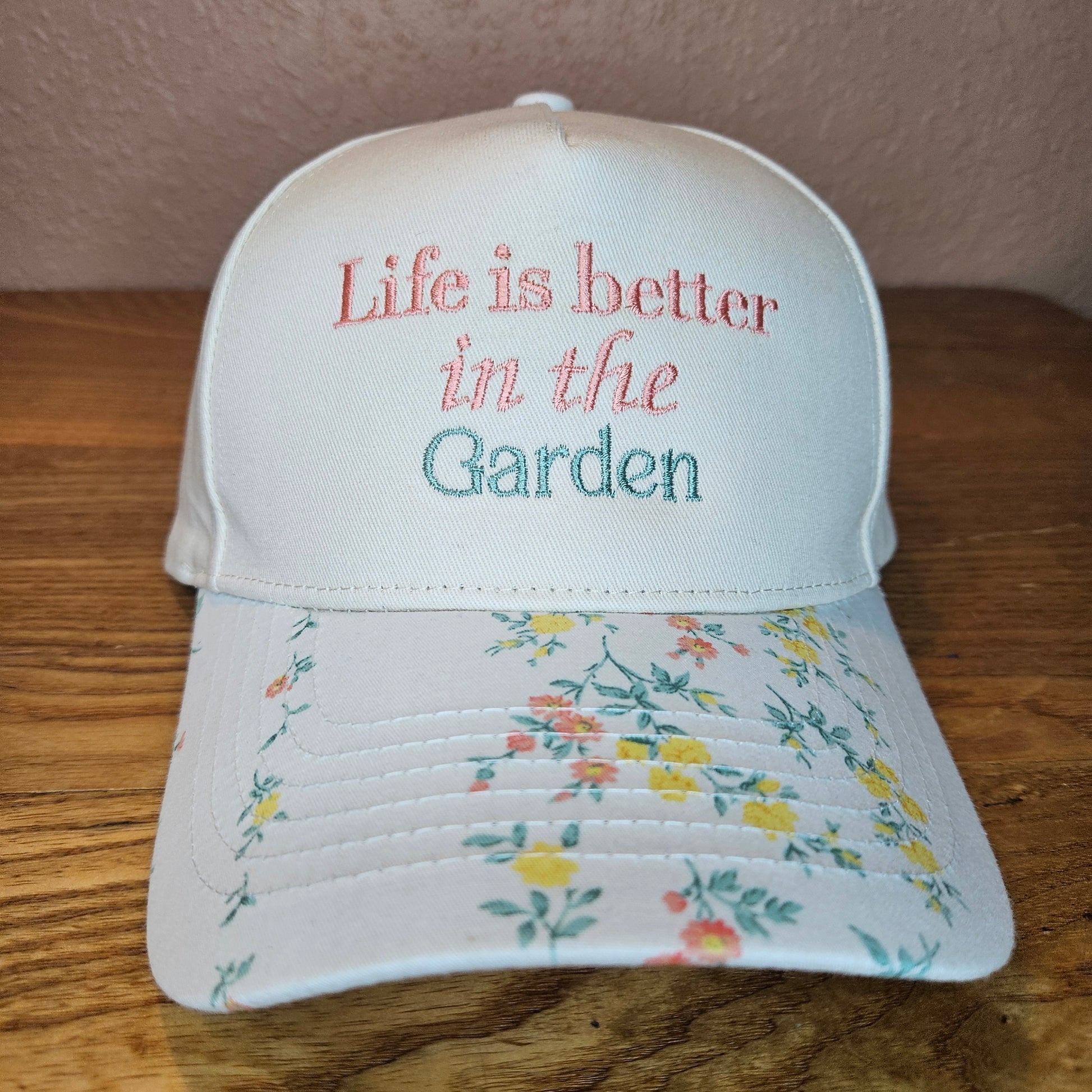 White cap with floral design and 'Life is better in the Garden' text on a wooden surface