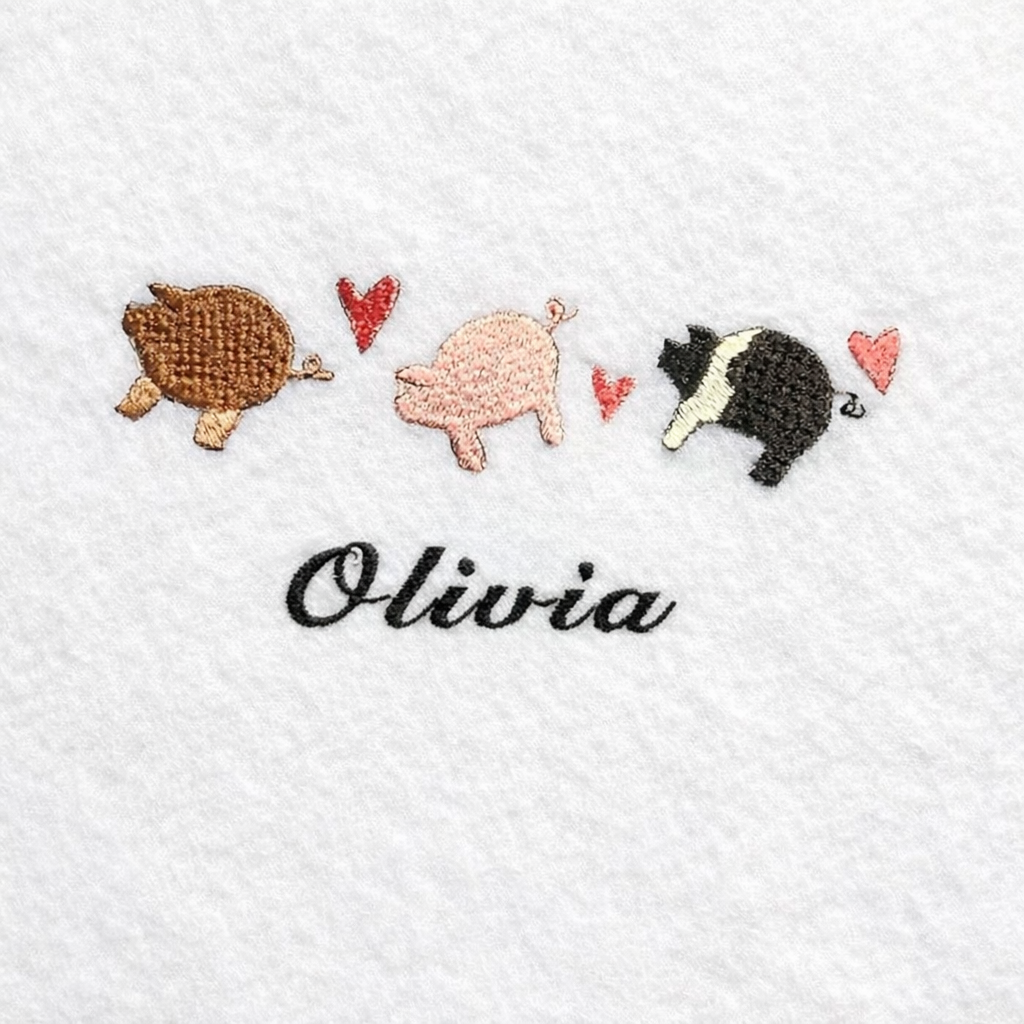 Embroidered design of three pigs and hearts on a white fabric with the name 'Olivia'.