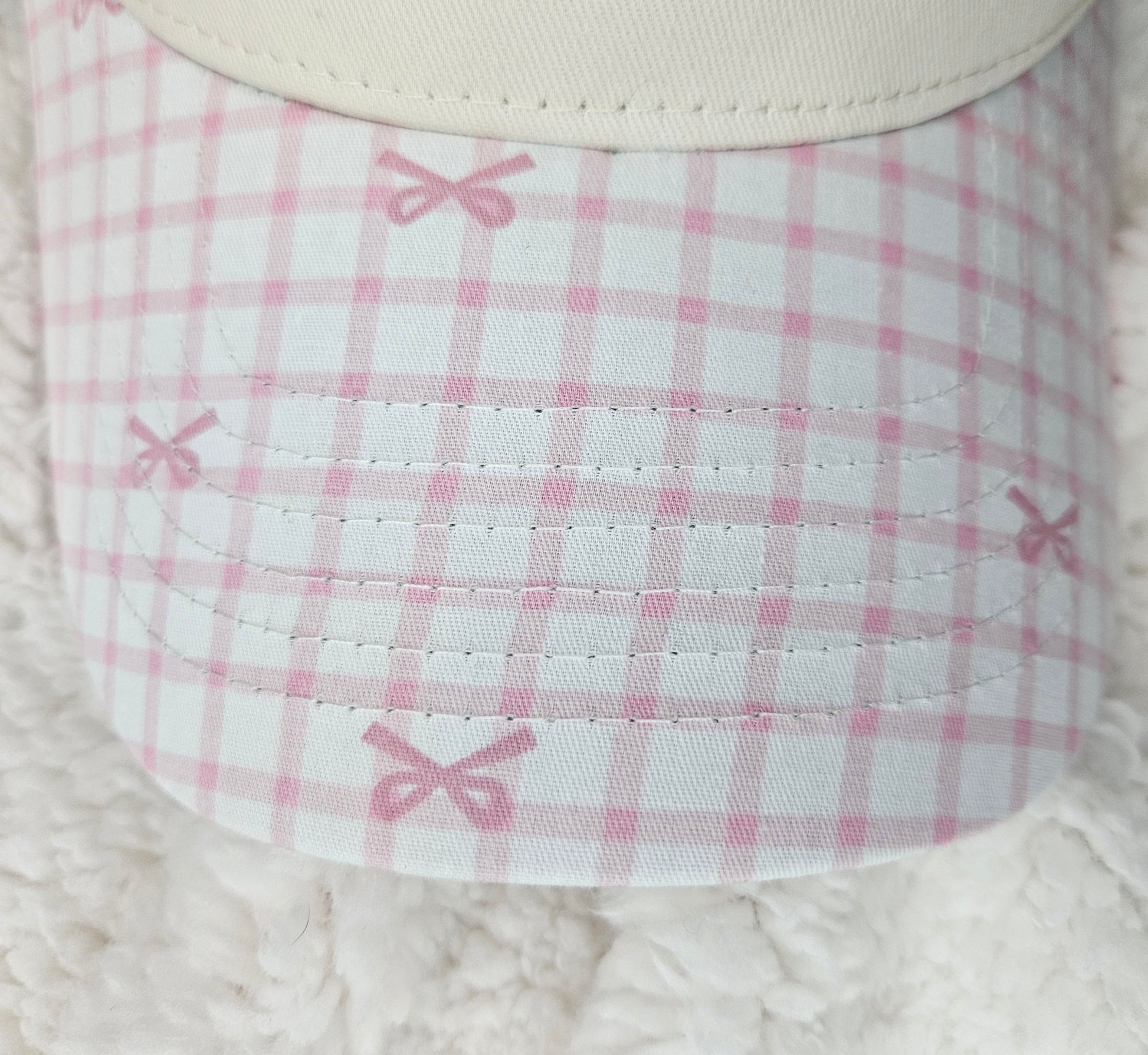 Close-up of a pink and white checkered bill of hat with bows on a textured surface